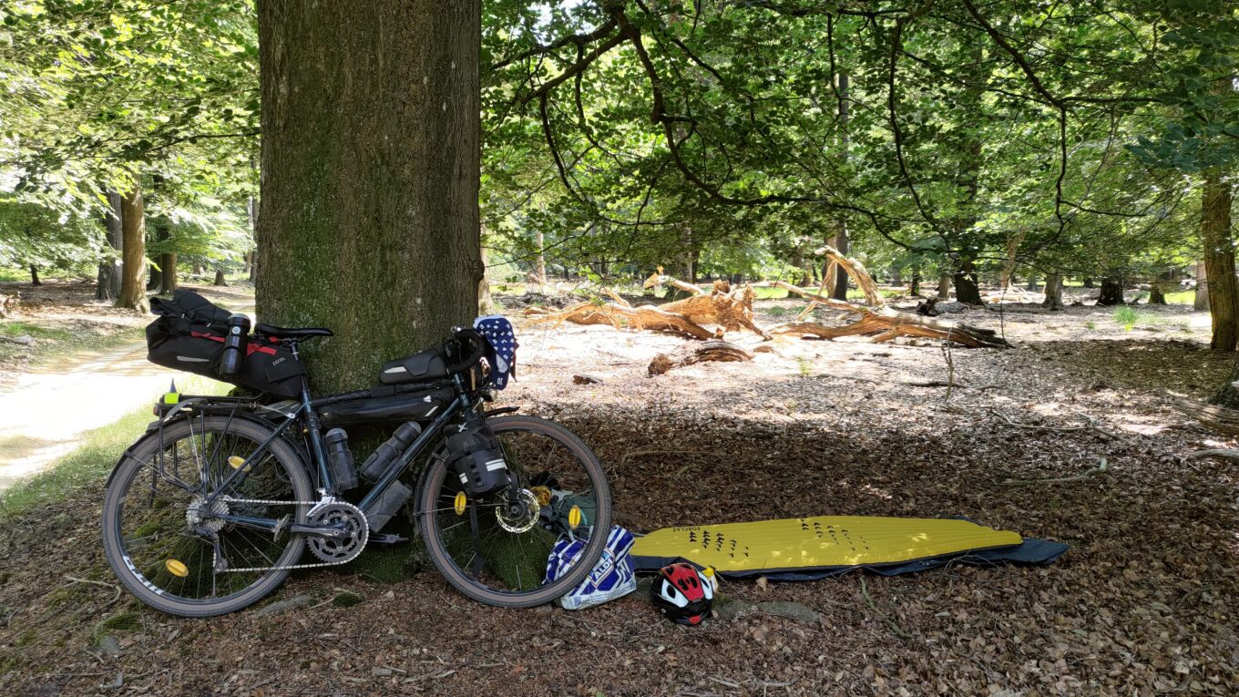 Dans les bois, un vélo posé sur un arbre. À ses pieds un matelas gonflable