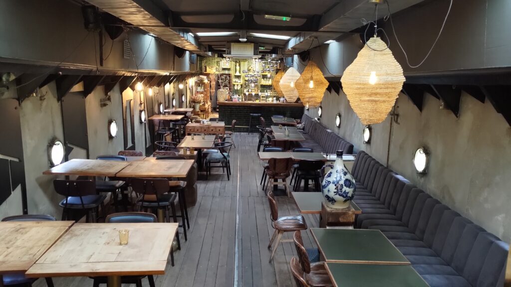 Intérieure d'une péniche transformée en restaurant. Ambiance cosy, tables rustiques en poids, grosses lampes en papier suspendues