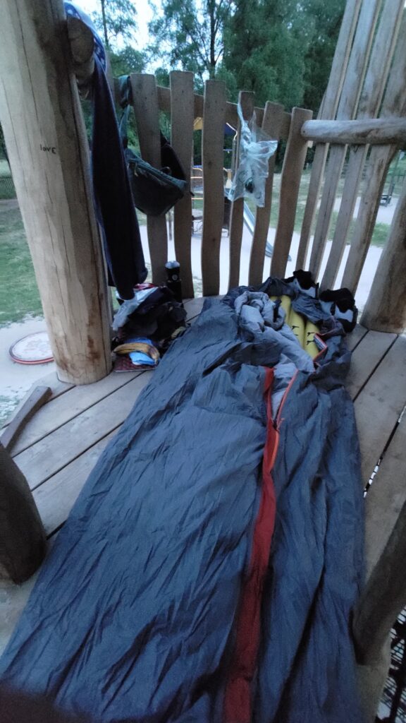 Installation de nuit, bivy, matelas, des affaires disposés à la tête. Le tout sur un planché en bois, on devine que l'on est en hauteur