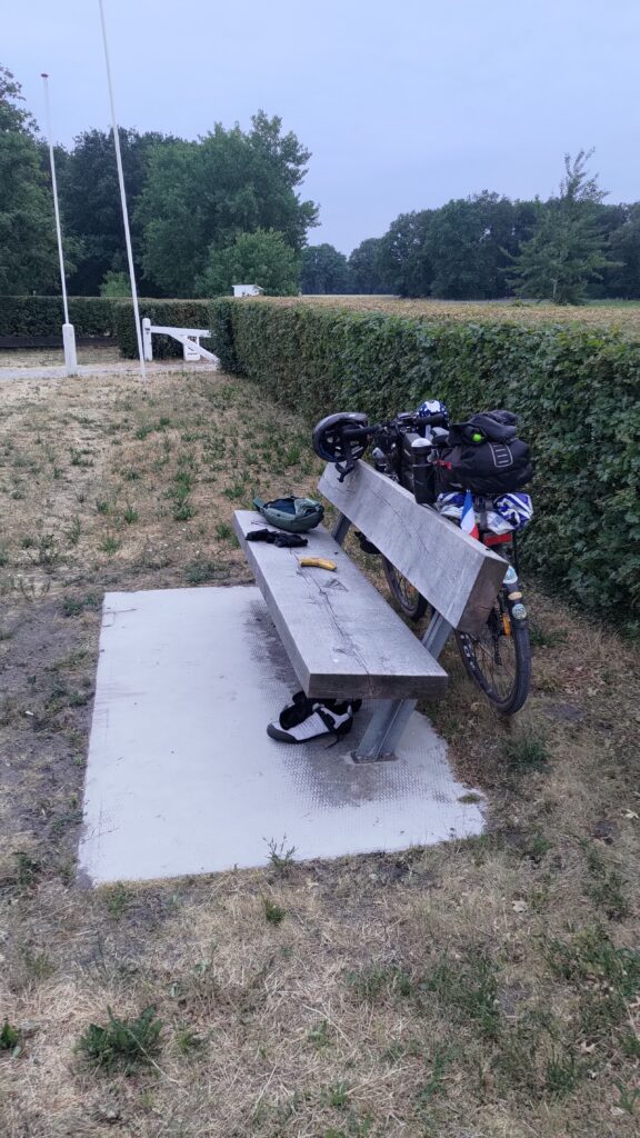 Un banc posé sur une dalle en béton, un vélo poser à l'arrière du banc. Il y a assez de place sur la dalle devant le banc pour s'allonger
