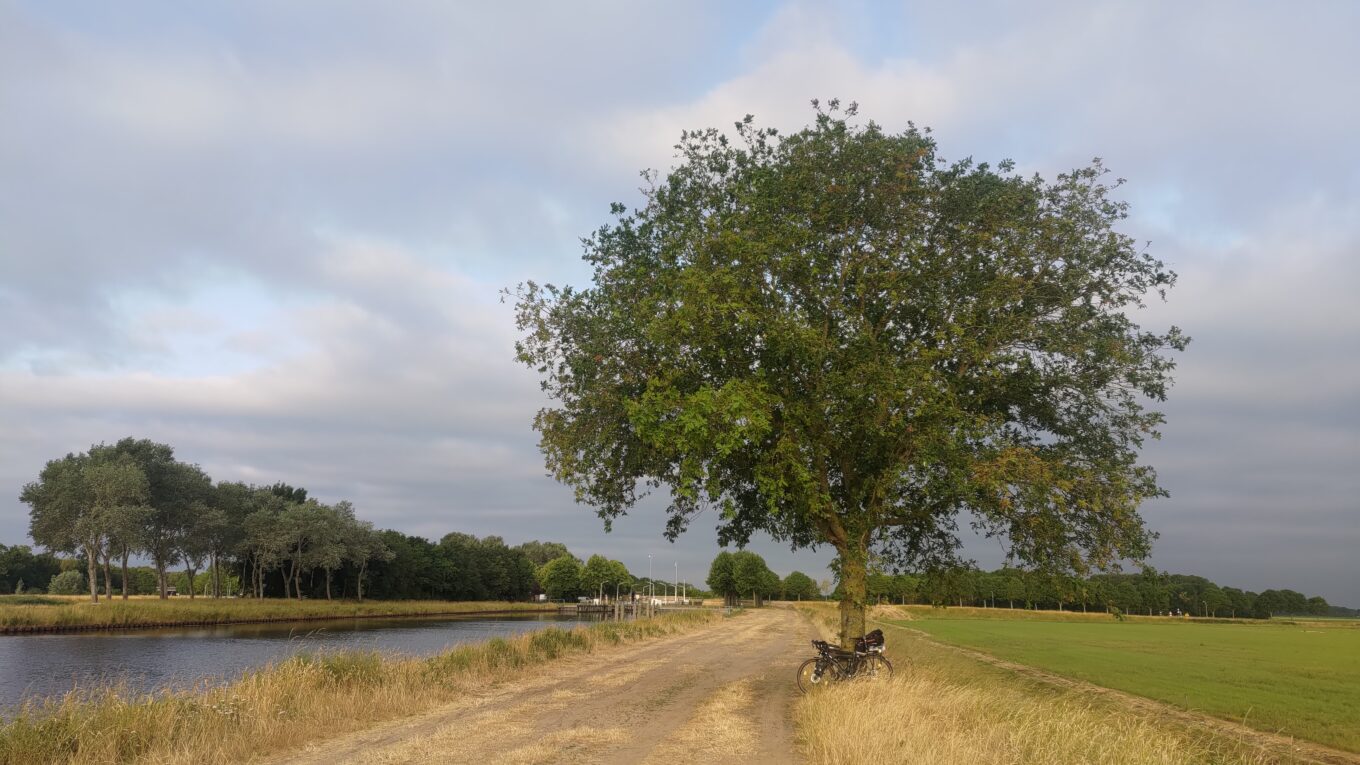 Large route de sable au centre de l'image. En parallèle à gauche un canal. Sur la droite un grand et dur lequel est posé un vélo