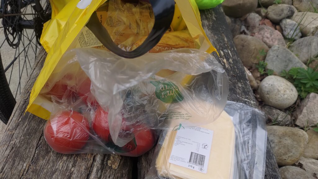Sac de provisions couché d'où sortent un sachet de tomates et du fromage en tranche
