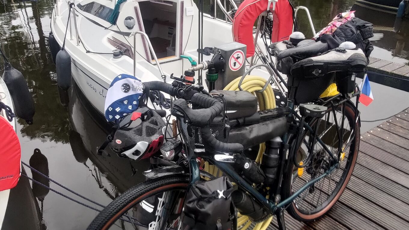Au premier plan un vélo sur un ponton, derrière un voilier habitable