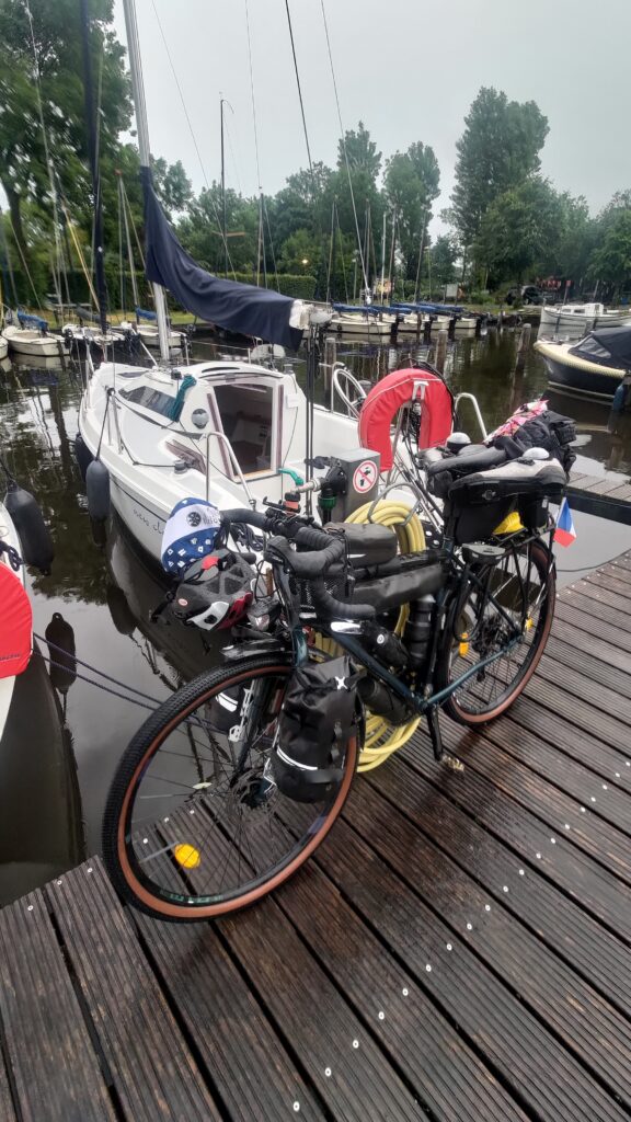 Au premier plan un vélo sur un ponton, derrière un voilier habitable