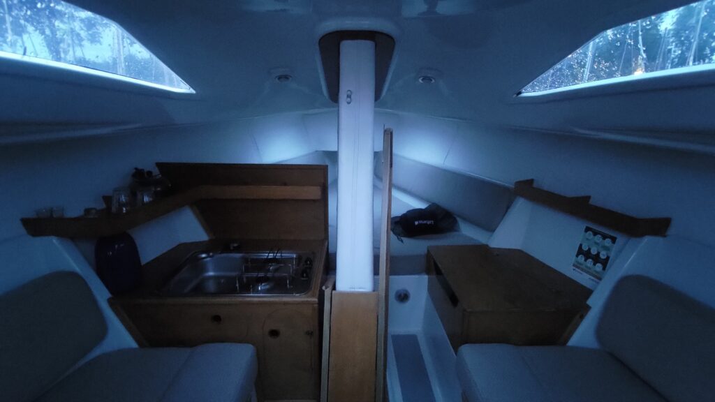 Intérieur d'un petit voilier habitable. Un coin cuisine, deux banquettes et un lit au fond