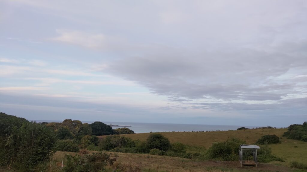 Paysage de campagne vallonné, on distingue la mer au loin