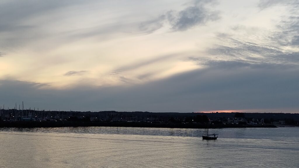 Couché de soleil sur la mer, derrière la ville. Un petit bateau à voile est visible