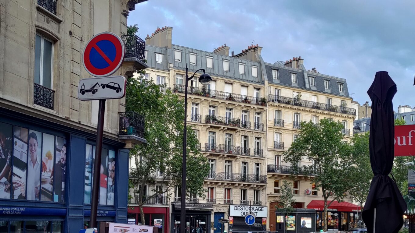 Vue d'une rue parisienne depuis la terrasse d'u' restaurant. Au premier plan un vélo pliant posé sous un panneau stationnement interdit, en haut un bon d'enseigne néon rouge où l'on lit restau japon.