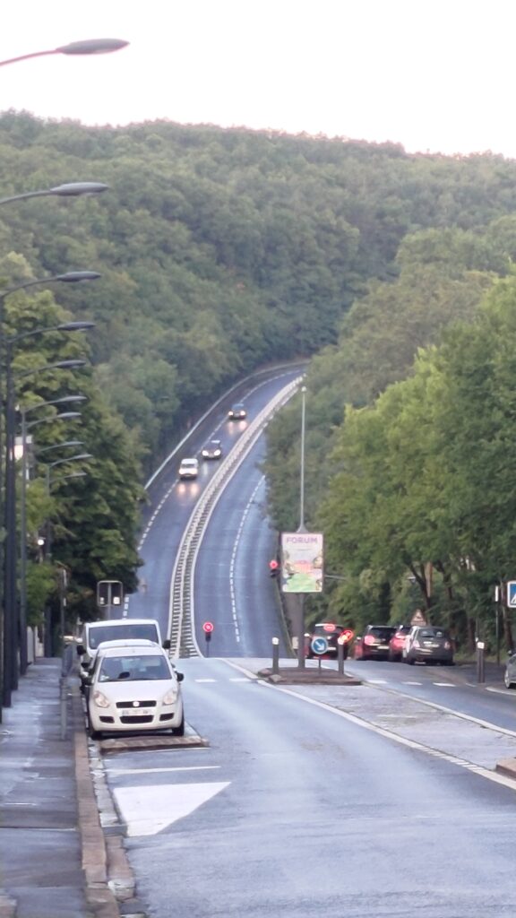 Côte de la rue du Pavé des Gardes vue de loin. La route faite une petite descente puis une très grande montée en 2x2 voies qui bouche la vue en tournant et se perdant dans la forêt