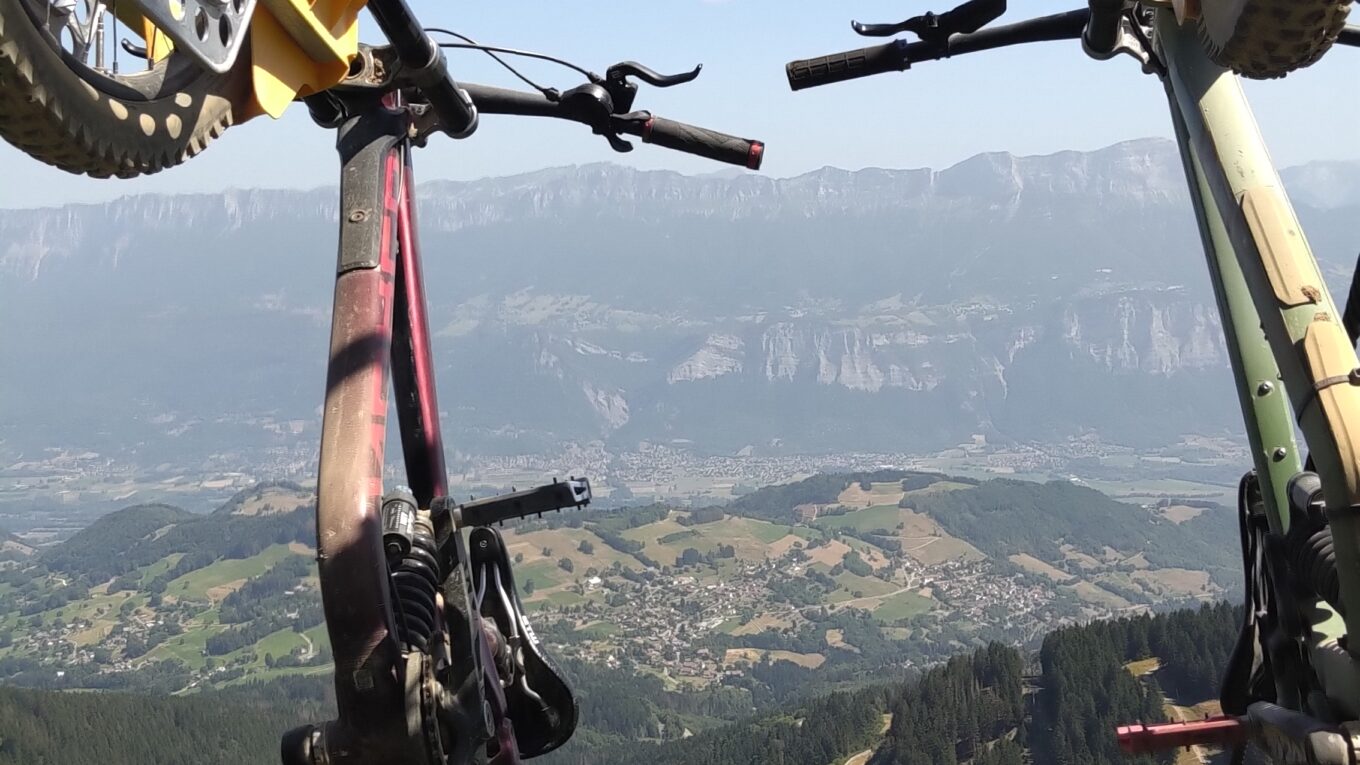 Deux VTT suspendus à un télésiège. Photo prise depuis le siège. En arrière plan la montagne (massif de la Chartreuse)