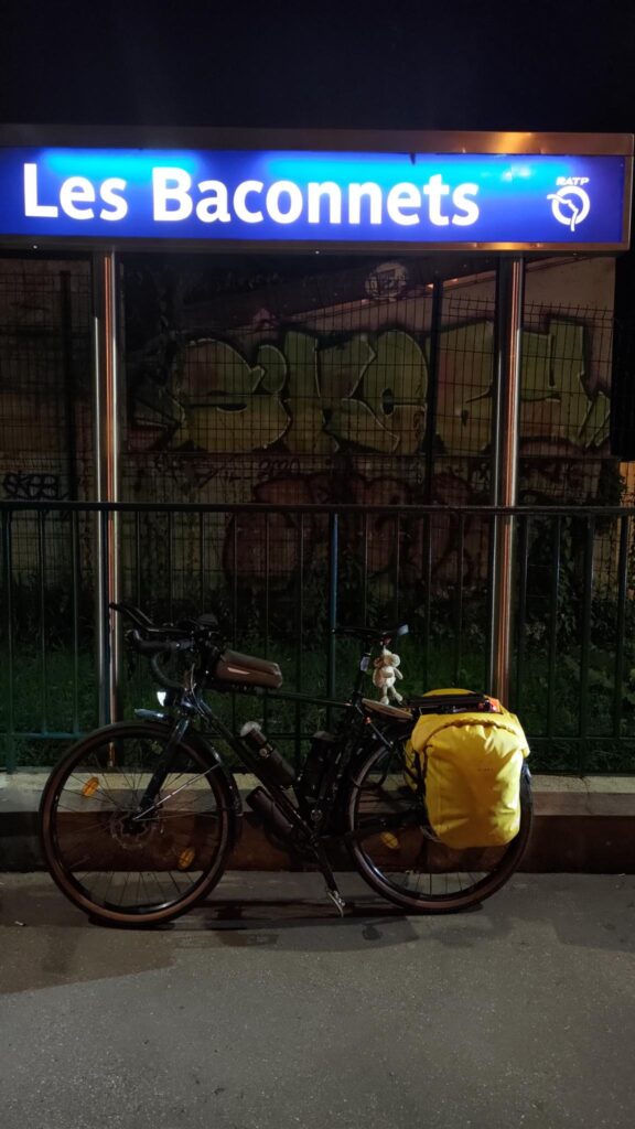 Photo de nuit. Un vélo est posé sous un panneau de RER illuminé en bleu à la station Les Baconnets