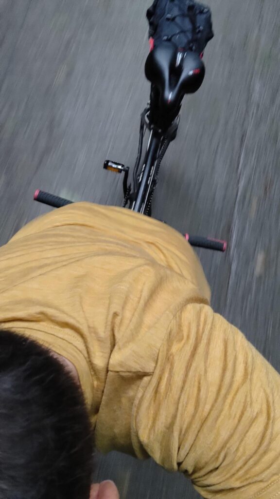 Un cycliste sur un tandem avec un t-shirt jaune. La vue en contre plongée est prise au-dessus de la tête du cycliste, On distingue la selle arrière du tandem inoccupée. Une sacoche de selle type gravel est installée.