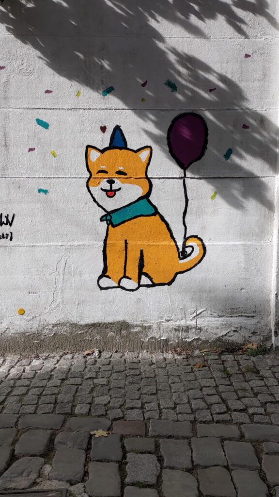 Fresque murale représentant un chien de la race Corgi dans un style bande dessinée. Le chien sourit. Il a sur la tête un tout petit chapeau bleu en triangle et un ballon gonflable attaché à la queue.