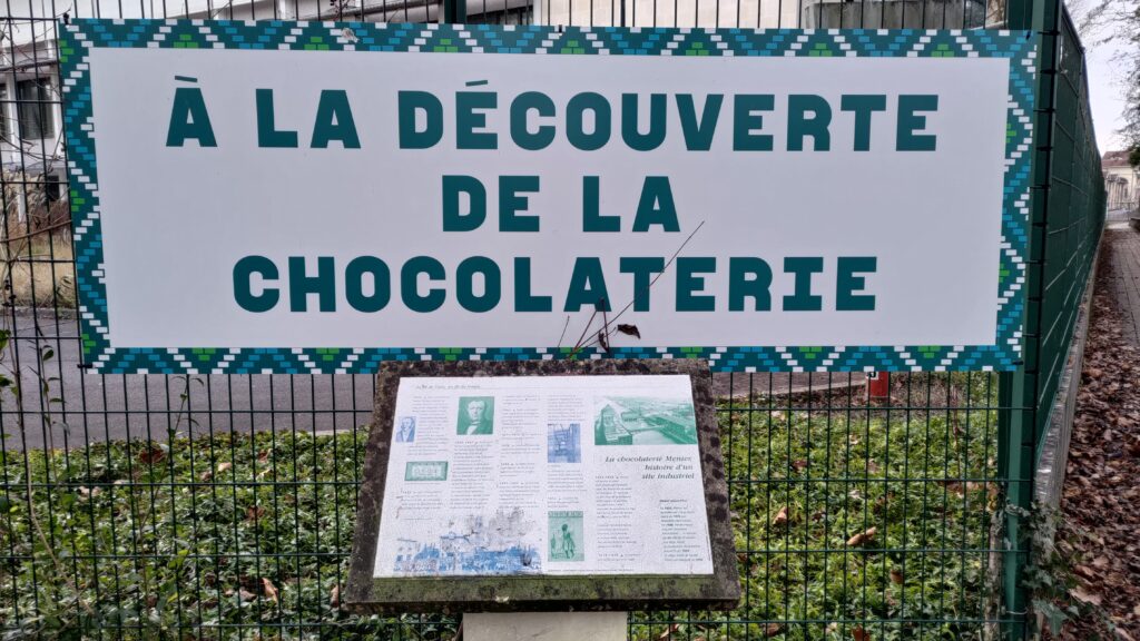 Grand panneau "À la découverte de la Chocolaterie" au-dessus d'un plus petit panneau contenant des explications