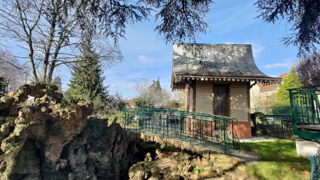 Dans un parc derrière la mairie d'Arpajon, un petit pont métallique devant une petite cabane avec un toit courbée