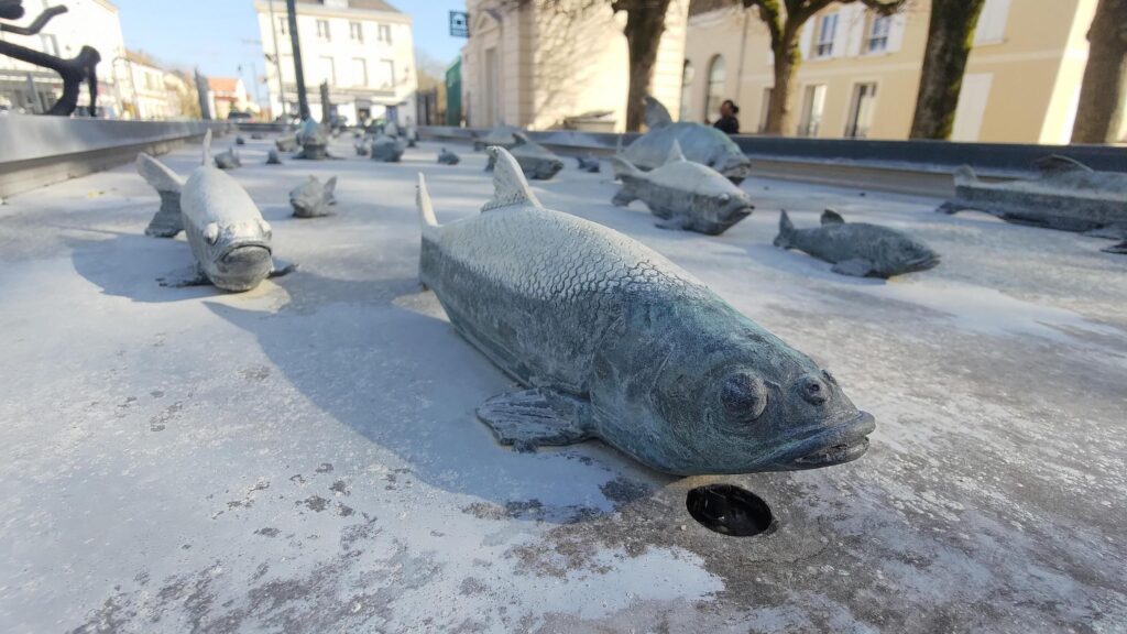 Un banc de poissons sculpté en bronze dans une fontaine sans eau