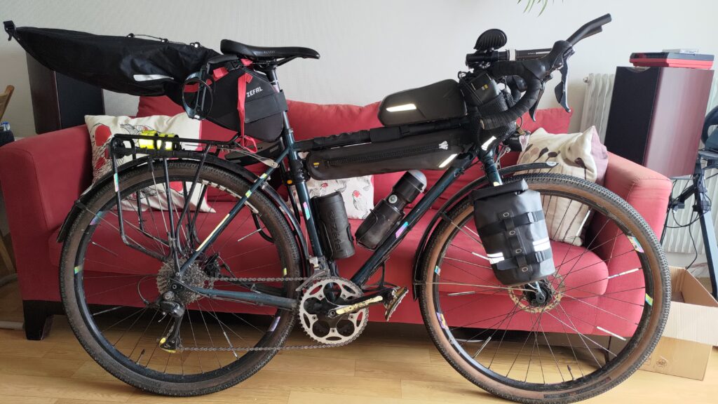 Vélo chargé de bagages type bikepacking appuyé sur un canapé dans un salon
