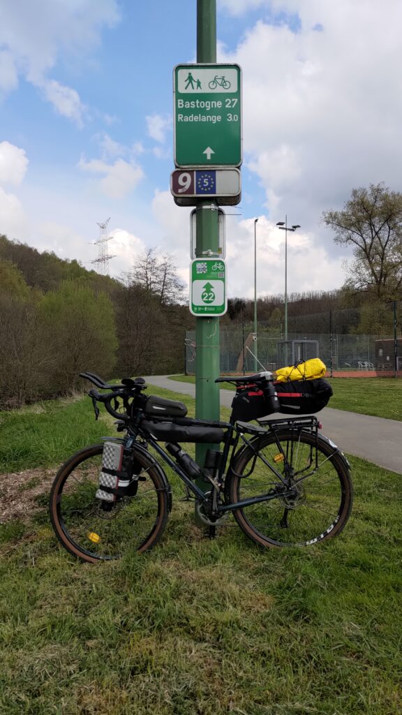 Vélo posé sur poteau avec panneau Veloroute EV5 et notamment Bastogne à 27km