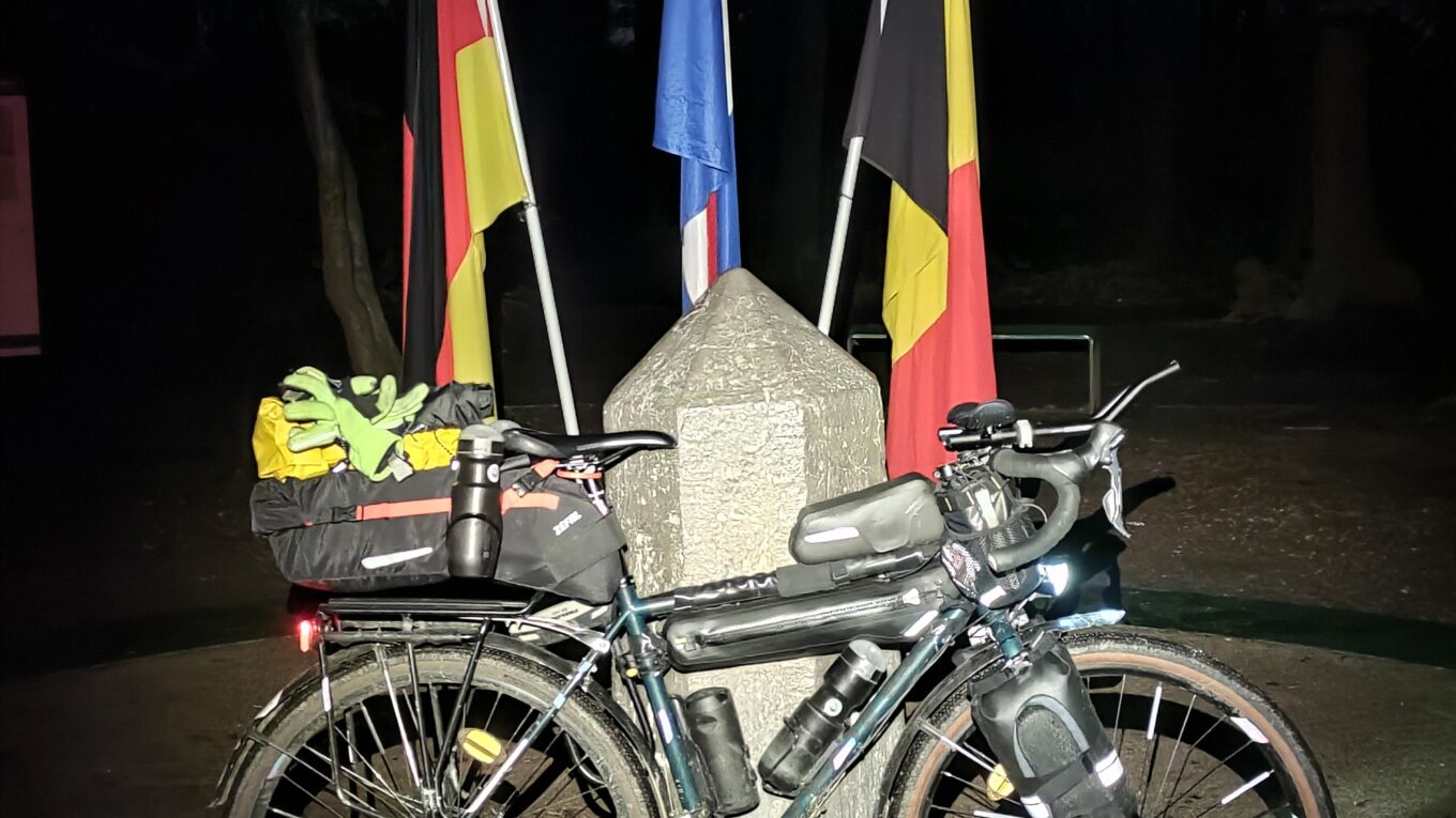 De nuit vélo devant le tripoint 🇩🇪 🇧🇪 🇳🇱 éclairage à la frontale, drapeaux des pays derrière
