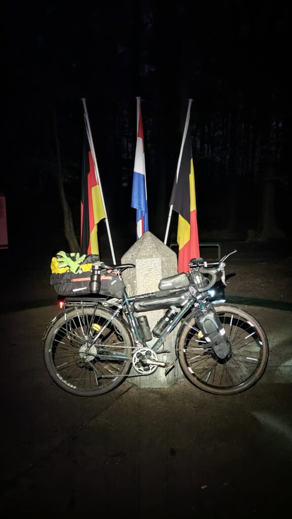 De nuit vélo devant le tripoint 🇩🇪 🇧🇪 🇳🇱 éclairage à la frontale, drapeaux des pays derrière