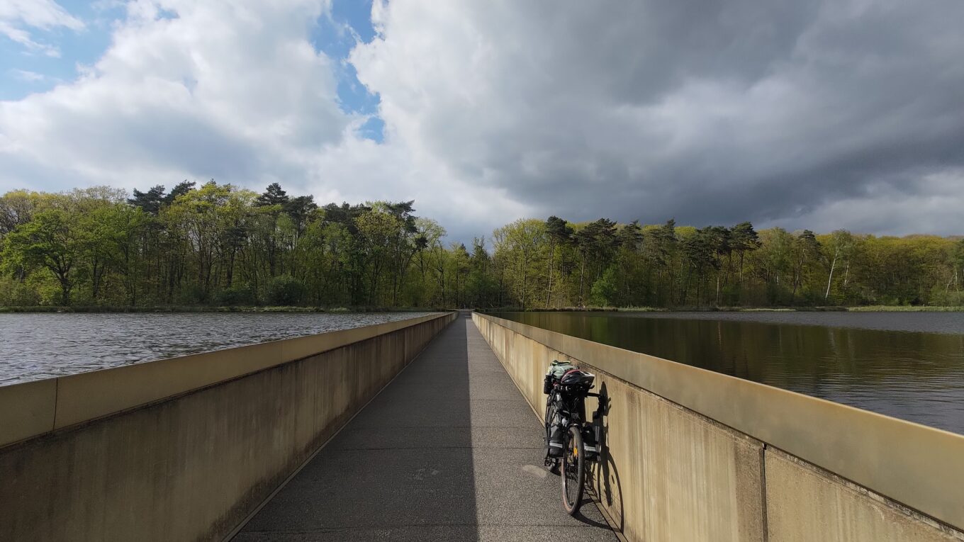 Un vélo posé le long d'un mur qui encadre une piste cyclable qui s'enfonce ainsi dans un lac