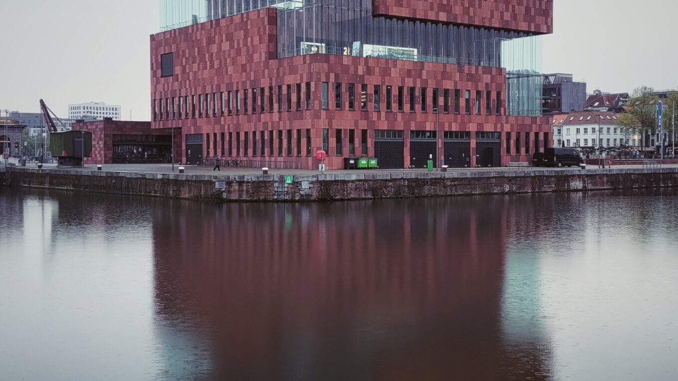 Vu du MAS (Museum aan de Stroom) à Antwerpen, grand bâtiment rouge et en verre qui se reflète dans l'eau du port