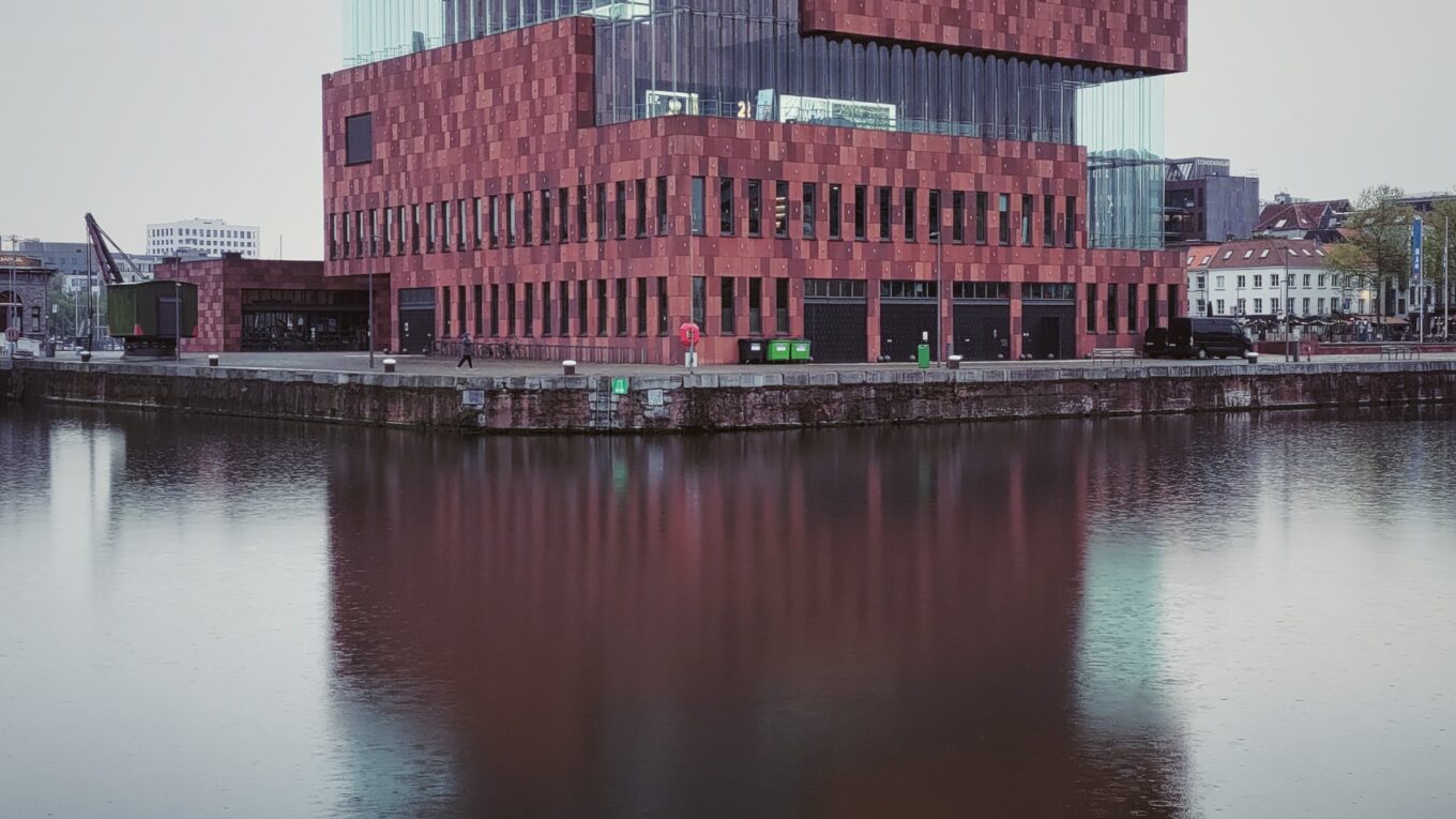 Vu du MAS (Museum aan de Stroom) à Antwerpen, grand bâtiment rouge et en verre qui se reflète dans l'eau du port