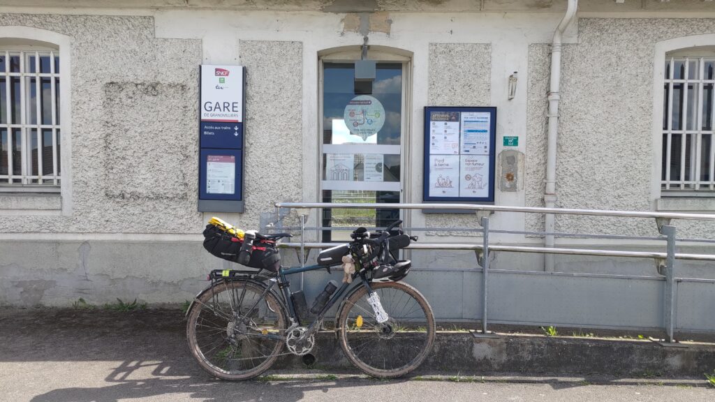 Vélo type gravel posé sur une rambarde devant la porte de la gare de Grandvilliers