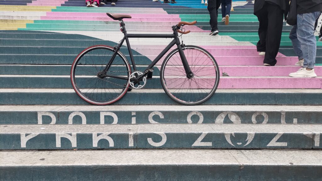 Vélo type single posé sur un grand escalier en pierre, les contre marches dessinent un logo pour les JO Paris 2024