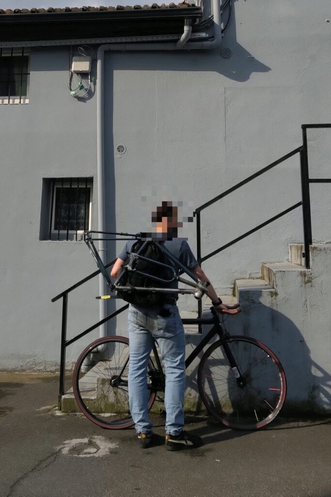cycliste de dos devant un vélo type single avec un sac à dos et un cadre de vélo accroché au sac à dos