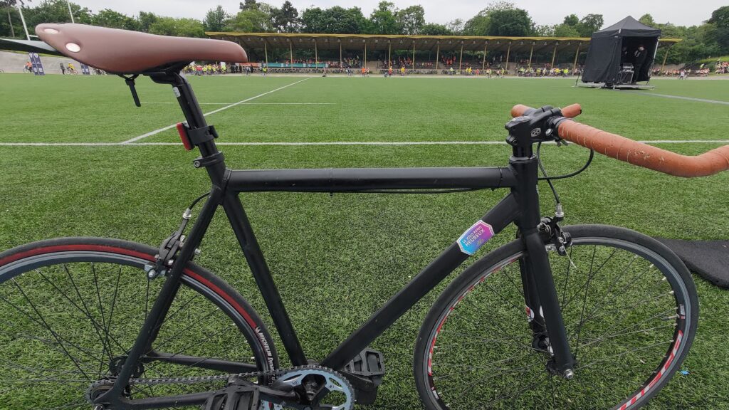 Vélo au premier plan, derrière une pelouse et au fond des tribunes anciennes