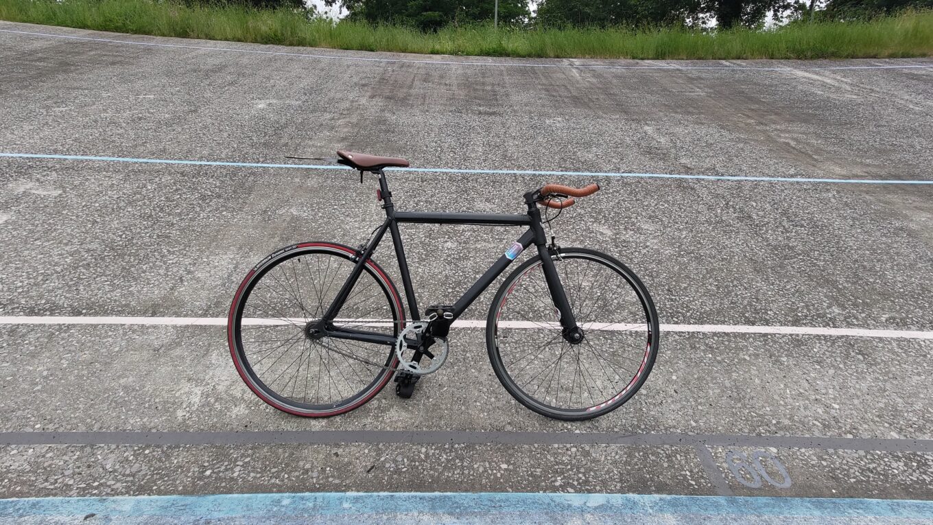 Vélo type single speed posé sur sa pédale sur la pente du virage d'une piste d'un vélodrome en extérieur