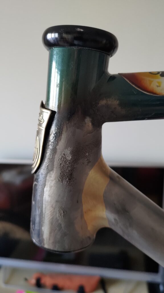 Gros plan sur la soudure entre le tube diagonal et la douille de direction d'un cadre de vélo. La soudure est récente, pas de peinture sur le nouveau type et peinture écaillée par la chaleur sur l'ancien cadre