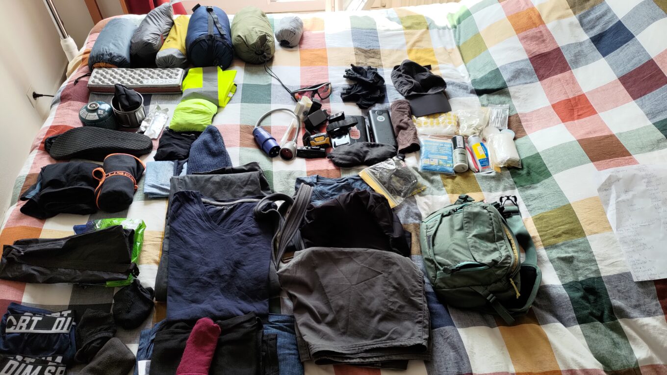 Des affaires, matériels de camping, vêtements, équipement électrique ou de toilettes disposés à plat sur un lit
