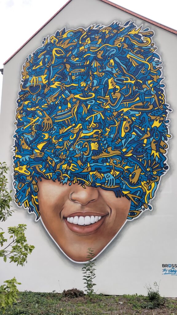 Un graphe sur tout un pignon de mur de maison représentant une personne dont les cheveux très volumineux masquent les yeux