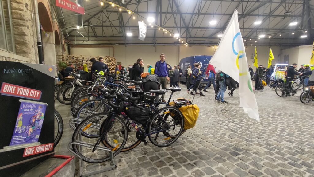 Dans un hangar, sol pavé, de très nombreux vélos dont l'un portant le drapeau olympique