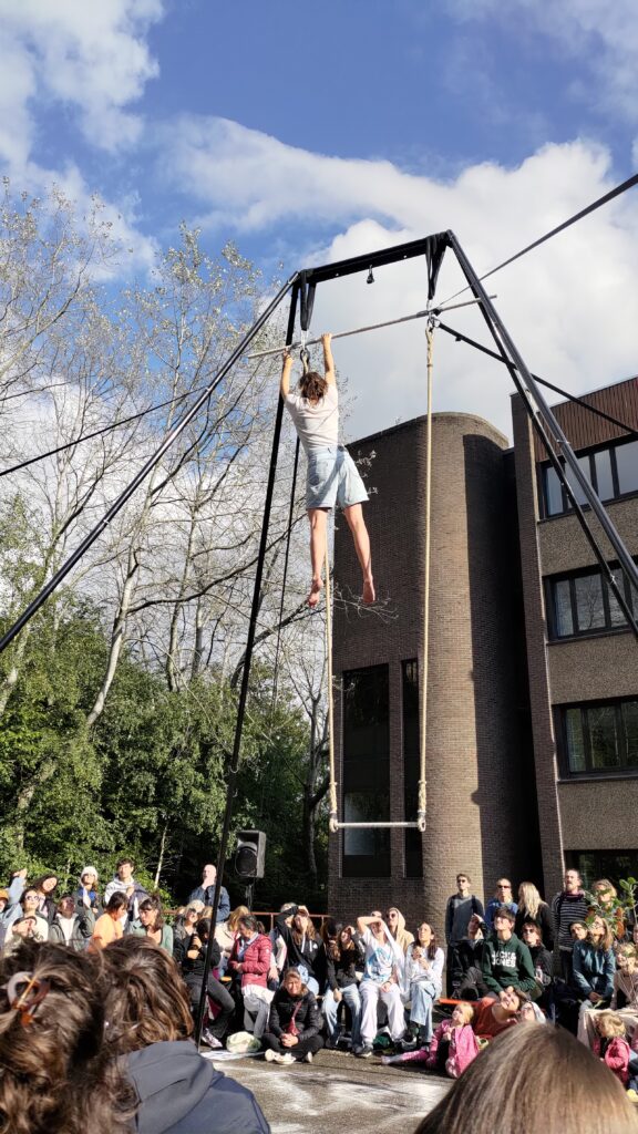 spectacle de rue, une structure d'environ 10 m de haut supporte un trapèze, l'artiste est suspendue au sommet de la structure, le public l'entoure