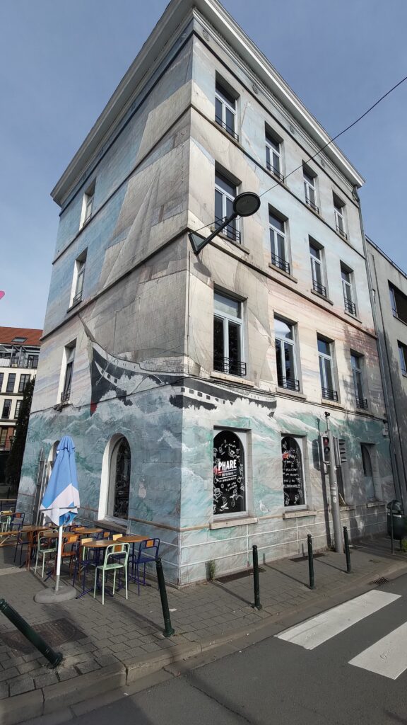 Un immeuble peint dans un angle de rue. C'est un bateau à voile à deux mats, historique, qui navigue sur une mer agitée.