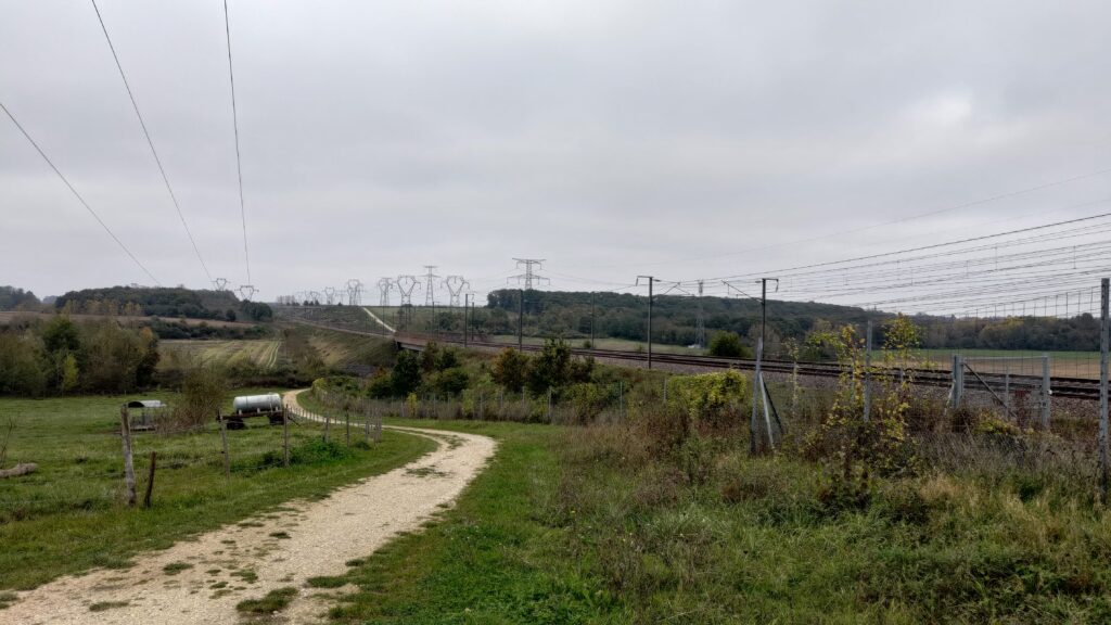Le long d'une voie verte passent un tgv et une ligne haute tensoie