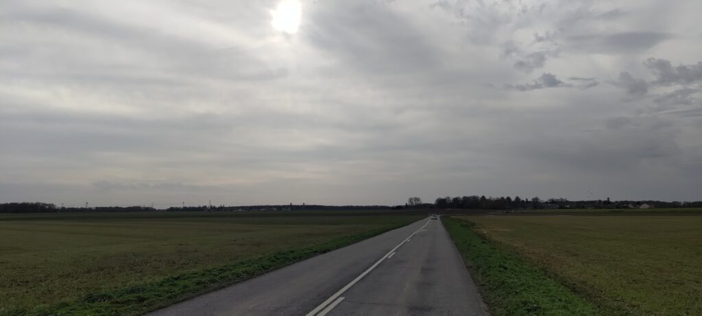 Une route à la campagne, des champs de part et d'autre de la route. Une voiture à l'horizon