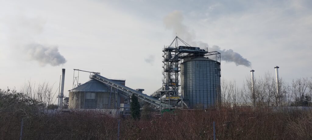 Un bâtiment industriel avec des structures métalliques très marqués, un grand tapis roulant et des cheminées fumantes de part et d'autre