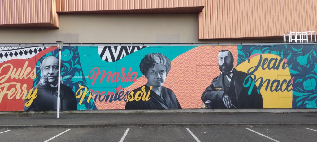 Un mur peint sur un gymnase scolaire représentant les portraits avec leur nom en grandes lettres de Jules Ferry, Maria Montessori et Jean Macé