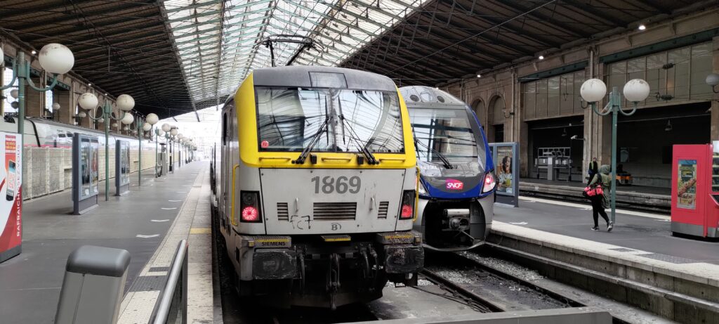 En tête de quai dans une gare une motrice aux couleurs de la sncb et derrière une sncf
