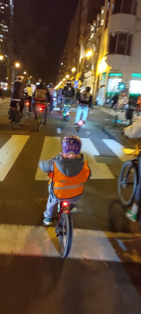 Un jeune enfant roule de nuit avec son gilet réfléchissant dans la foule de la Critical Mass