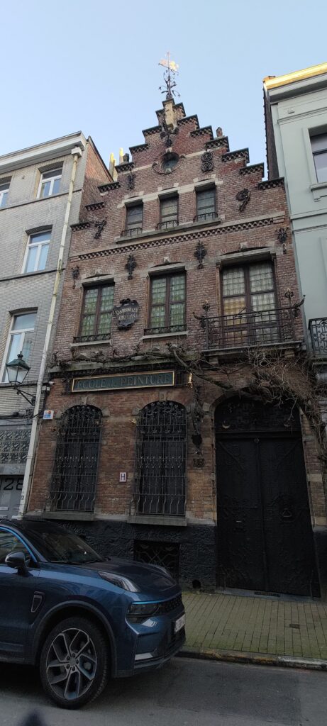 Une vieille maison en briques, balcon fer forgé, girouette métallique au sommet, en ville à Bruxelles
