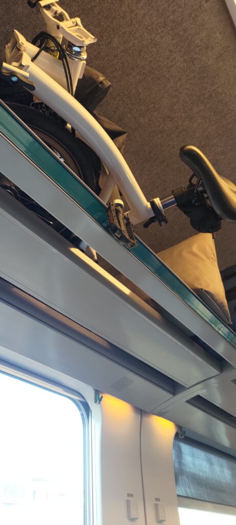 Un vélo plié posé dans un porte bagages au-dessus des passagers (que l'on ne voit pas) dans un train