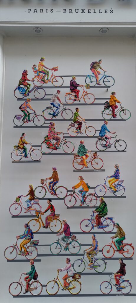 Sur une façade de boutique, pleins de vélos et cyclistes dessinés, vus de profil, au-dessus écrit Paris-Bruxelles