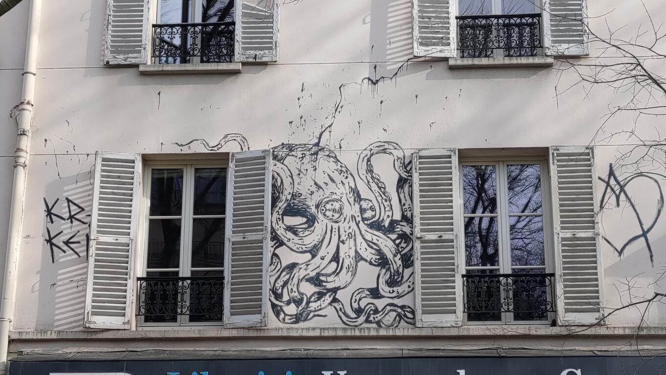 Façade d'un immeuble parisien avec des fenêtres équipées de persiennes en bois ouvertes, entre les deux fenêtres dessin d'un poulpe assez réaliste