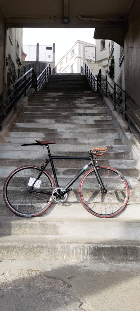Un vélo type single posé au pied d'une longue volée de marches qui montent