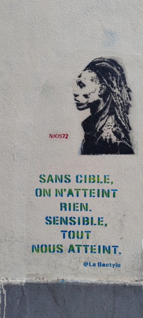Pochoir représentant une personne à cheveux long vue de profil, signature "NJO972" et texte "SANS CIBLE, ON N'ATTEINT RIEN. SENSIBLE, TOUT NOUS ATTEINT.", signature "@La Dactylo"